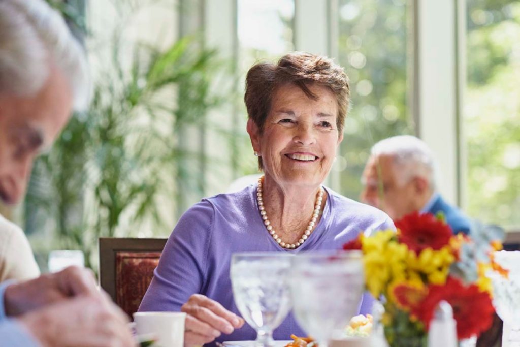 elderly woman smiling while eating lunch at her retirement home