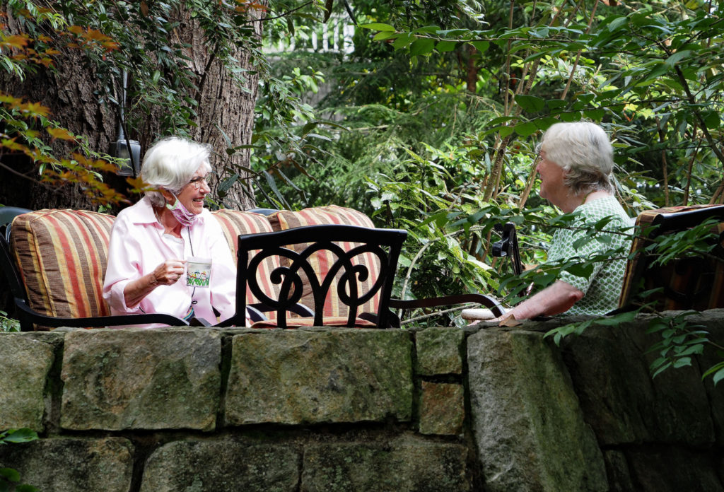 two elderly women drink coffee outside their retirement community