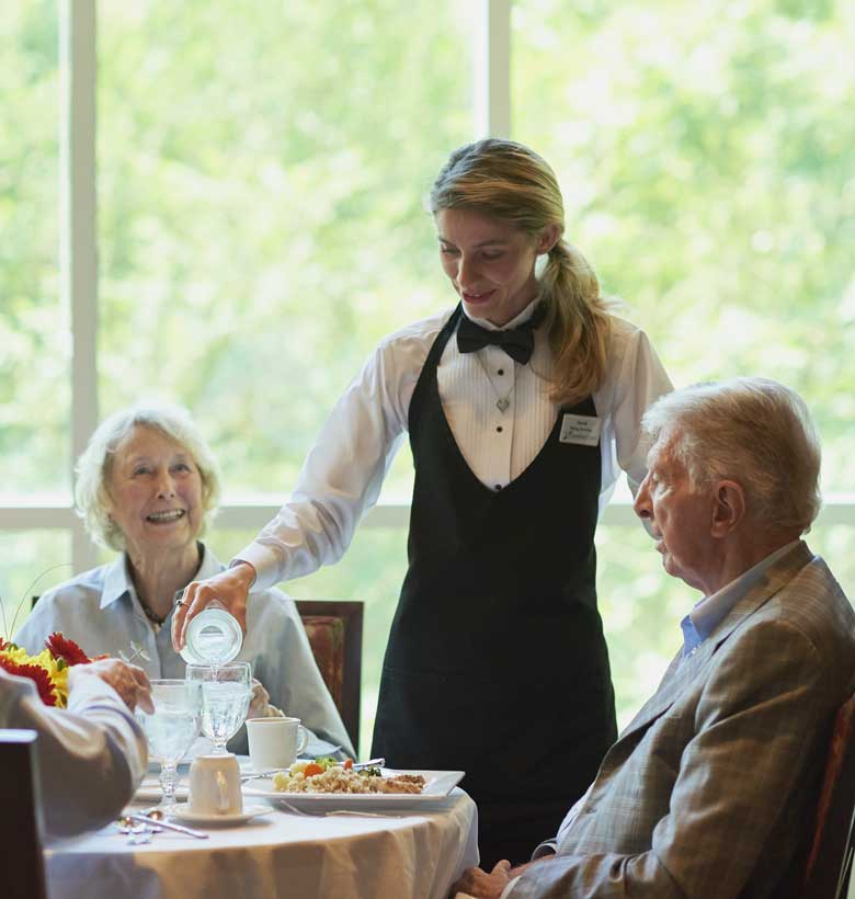 Waitress filling up a water glass for seniors dining together